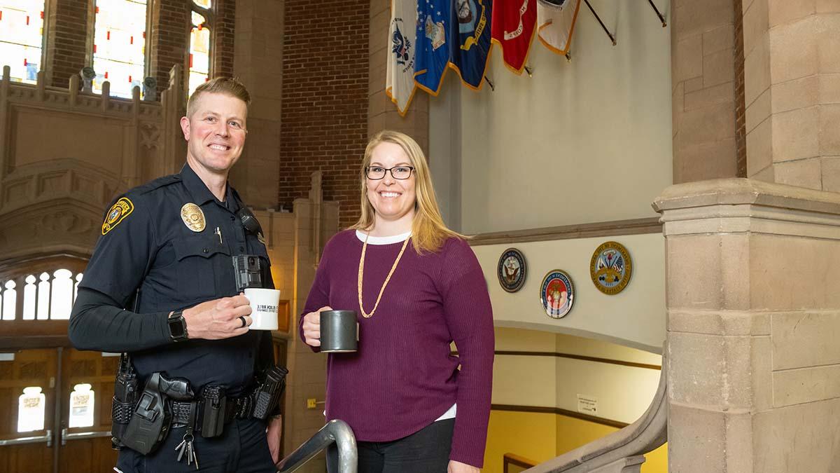 校友 and 操作的教育 scholarship recipients Jennifer Tengono 杰森·豪斯 hold coffee mugs in the lobby of the Memorial Gym