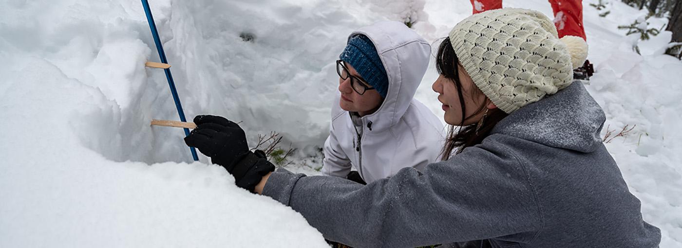 两个学生用冰棒棒测量雪坑中雪层之间的距离.